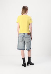 Gul farge bomulls t-skjorte, kombinert med slitte denimshorts med frynset kant, og svarte ankelboots med hæl. Enkelt design, avslappet passform.