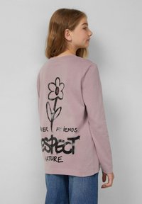 Roze langemouw shirt met een zwart bloemenafbeelding en de tekst "RESPECTEER DE NATUUR" en "KRAFT VRIENDEN." Zacht katoen, relaxte pasvorm.