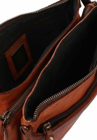 Bruine leren tas met twee compartimenten, voorzien van zwarte textielvoering en dubbele ritsen. Gecarveerde buitenkant met een gladde afwerking.