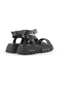 Sandalias de plataforma negras con correas anchas, cierre de hebilla en el tobillo y suela texturizada. Acentos de hardware plateado notables a lo largo de la base.