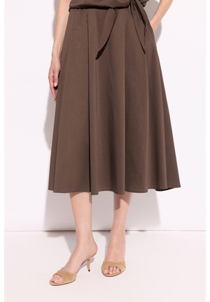 Brązowa spódnica midi z wiązanym paskiem w talii, noszona z beżowymi sandałami na obcasie z odkrytymi palcami na jednolitym jasnym tle.