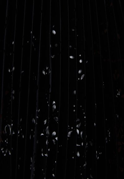 Fekete redőzött szövet kivágott virágmintákkal; sima textúra; a fény és árnyék játéka látványosan bonyolult mintázatot teremt.