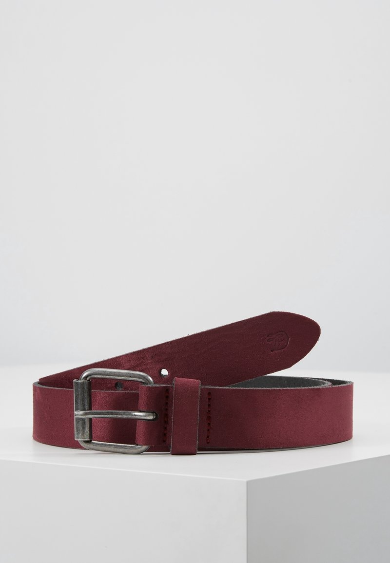 Ceinture en cuir rouge foncé avec boucle en métal argenté, enroulée sur une surface blanche sur un fond gris clair uni.