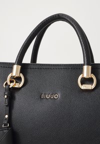 Borsa in pelle nera con hardware dorato, doppi manici, logo impresso e texture liscia. Presenta un compartimento con zip.
