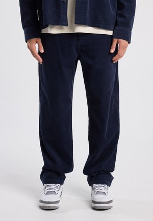Navy corduroy broeken met een relaxte pasvorm, met verticale ribbels en een lichte glans. Gepaard met witte sneakers voor contrast.