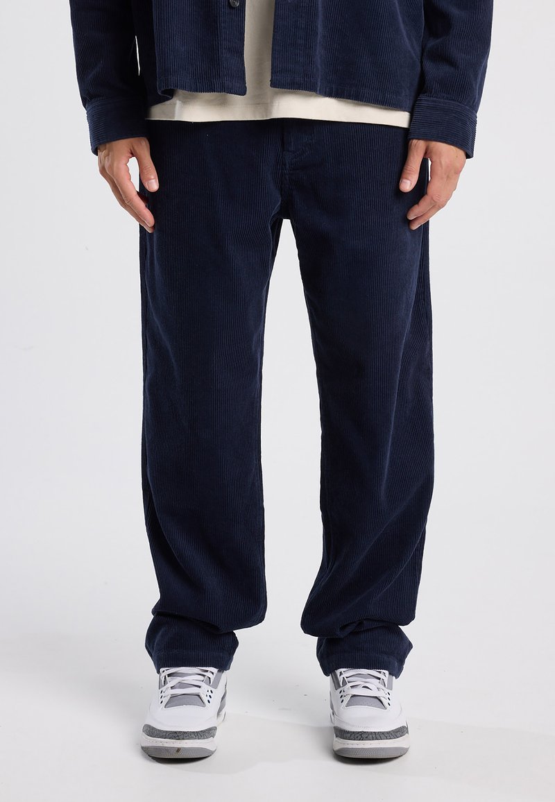 Navy corduroy-housut, joissa on rento malli ja pystysuorat urat sekä hienoinen kiilto. Yhdistetty valkoisiin tennareihin kontrastiksi.