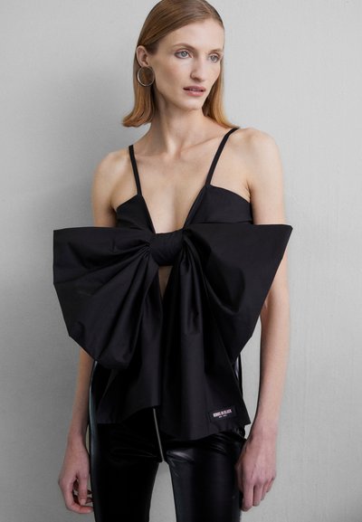 Black sleeveless top with a large bow detail at the front, made from a smooth fabric. Features thin straps and a keyhole cutout.
