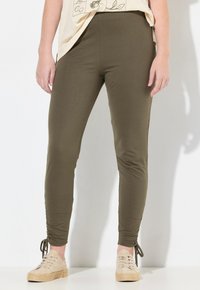 Olivgröna leggings med en figurnära design, featuring sidofåll och justerbara snören vid anklarna. Mjukt, töjbart tyg.