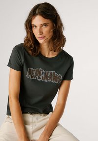 Camiseta de algodón gris oscuro con un gran gráfico metálico de "PEPE JEANS" en tonos caqui y dorados. Manga corta y diseño clásico de cuello redondo.