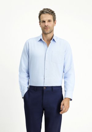 Camisa de manga larga azul claro con cuello abotonado y bolsillo en el pecho, combinada con pantalones navy con cierre de botón.
