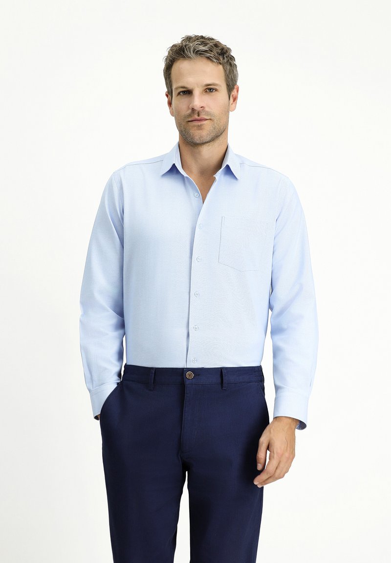 Camicia azzurra a maniche lunghe con colletto button-down e taschino, abbinata a pantaloni blu navy con chiusura a bottone.