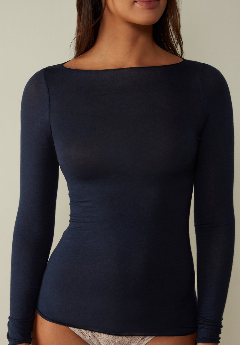 Marineblauw longsleeve shirt van een zachte, rekbare stof. Kenmerkt zich door een bootnek en een aansluitende pasvorm. Glad textuur, minimale details.