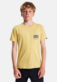 Žluté bavlněné tričko s kulatým výstřihem, krátkým rukávem a černobílým grafickým logem na levé straně hrudníku.