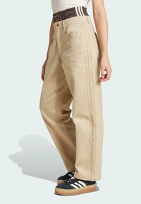 Béžové nohavice so širokými nohavicami a vysokým pásom, zdobené leopardím vzorom a tromi vertikálnymi pruhmi. Vyrobené z pevnej látky s jemnými švrčkami.