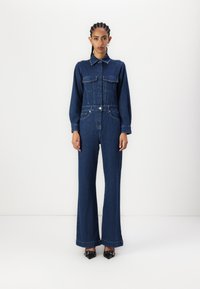 Denim jumpsuit met een kraaghals, lange mouwen en twee voorkomende zakken. Donkerblauwe kleur, wijde pijpen, accentueert met een ceintuur in de taille.