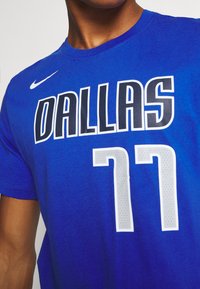Uomo che indossa una maglia da basket blu di Dallas con il numero 77 e il logo Nike bianco sul petto.