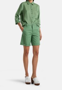 Světlý zelený dlouhý rukáv košile a odpovídající kraťasy ke kolenům, oba vyrobené z hladkého materiálu. Nesené s bílými dřev�áky s dřevěným podpatkem.