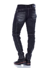 Schwarze Denim-Jeans mit Slim-Fit, mit kontrastierendem weißen Nähten, Reißverschlusstaschen und einem verwaschenen Design an Oberschenkeln und Rückseite.