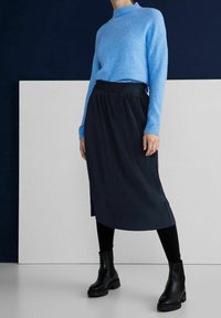 Light blue knit sweater with a high neckline paired with a pleated dark blue skirt and black ankle boots. Smooth texture and fitted silhouette.