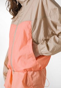 Let jakke i beige og koral, med lynlås foran, elastiske manchetter og sidelommer samt justerbar talje med snore.