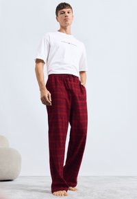 Un pantalon de pyjama à carreaux rouges avec une taille élastique et un cordon de serrage, associé à un t-shirt à manches courtes blanc uni avec un logo.