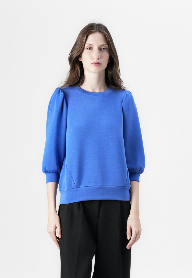 Pullover blu con scollatura rotonda, maniche a sbuffo e orlo a coste. Realizzato in tessuto testurizzato, presenta accentuazioni sui pannelli laterali.