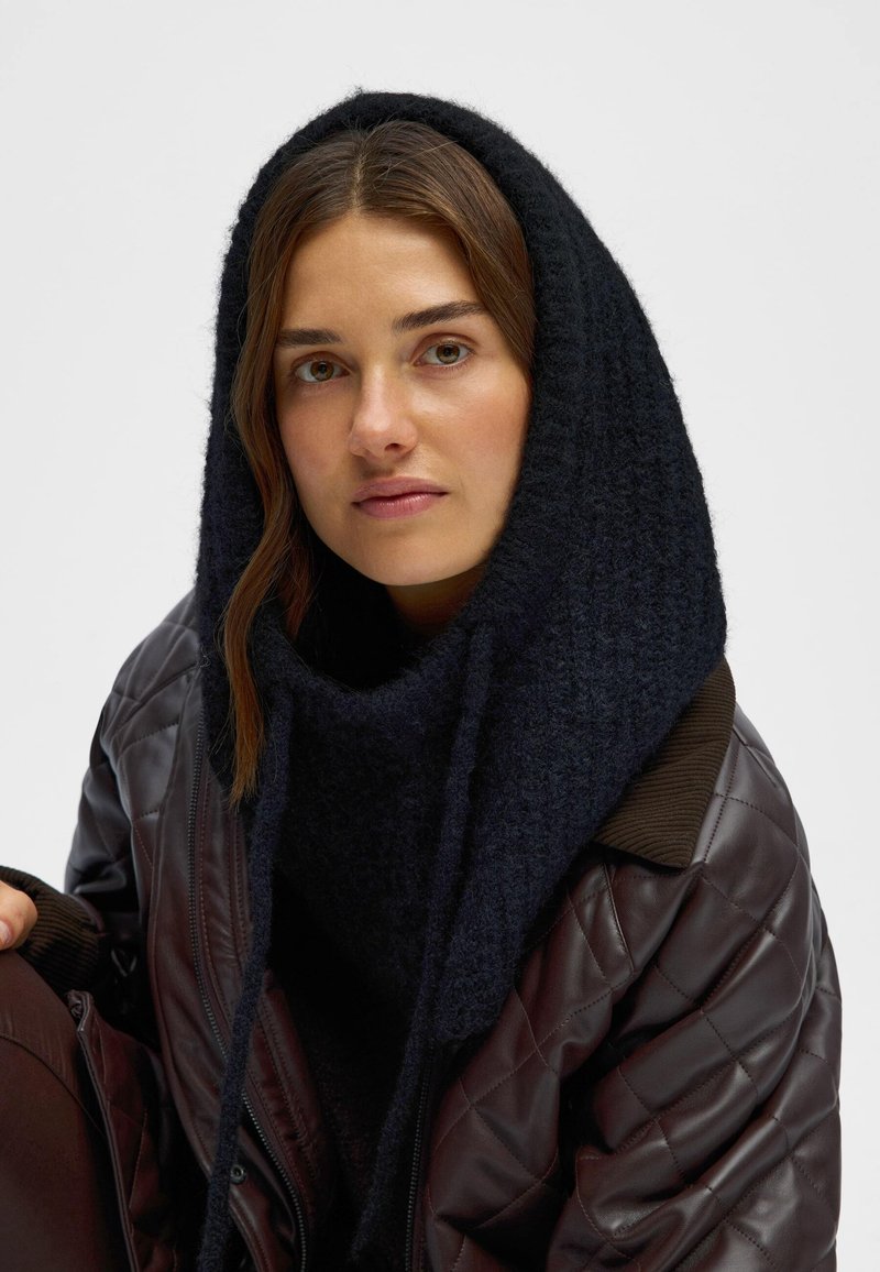 Mörk marinblå stickad huva/scarf lagd över en brun kviltad jacka med ribbad krage, som har en mjuk textur och rikligt med volym.