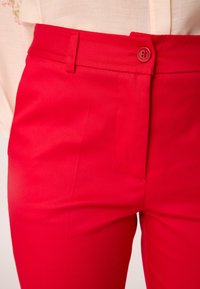 Rode, getailleerde broek gemaakt van gladde stof, met een enkele knoopsluiting en een zijzak. Netjes afgewerkte naden en een taillering ontwerp.