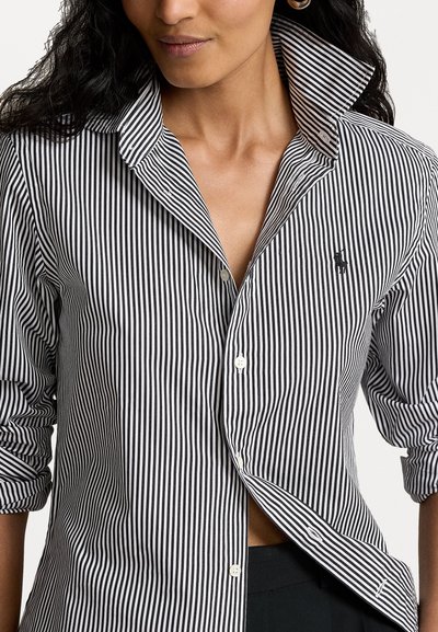 Chemise à rayures noires et blanches à col évasé, avec des manches longues retroussées aux poignets et un petit logo brodé.