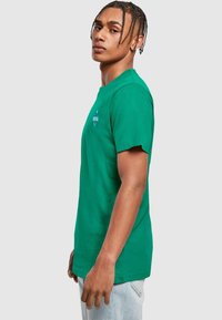 Green cotton T-shirt with short sleeves, a crew neckline, and a small graphic print on the chest. Simple, relaxed fit, smooth texture.