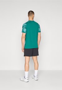 Camiseta deportiva color turquesa con mangas estampadas, combinada con pantalones cortos negros. La camiseta tiene un escote redondo y aberturas laterales.