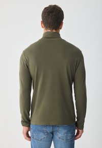 Tricou polo cu mânecă lungă, de culoare verde măsliniu, cu guler, textură fină și siluetă ajustată, asortat cu blugi din denim albastri.