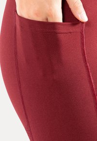 Bordeaux rode stretchleggings met een zijzak, voorzien van vlakke naden en een gladde textuur. De stof lijkt elastisch en aansluitend.