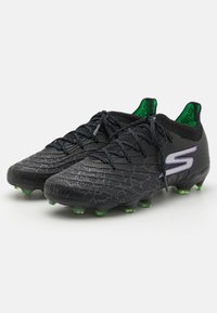 Svarte fotballsko med teksturert overdel, grønne detaljer og piggstuds. Snørene er svarte og viser en fremtredende logo på siden.