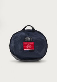 Navy mesh duffel bag with black accents and a red label. Round shape, zip closure, and a top handle for convenient carrying.