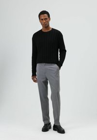 Zwart geribd trui, lichtgrijze broek en zwarte schoenen. Eenvoudige, gestructureerde trui met een strakke pasvorm en een gedempaletten kleur.