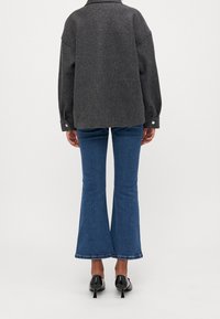 Szara, oversizeowa kurtka z mieszanki wełny z opuszczonymi ramionami i rękawami z zapinanymi mankietami, połączona z rozszerzanymi niebieskimi dżinsami i czarnymi butami na obcasie.