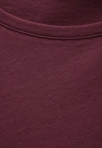 Bordeauxfarbene Baumwollstoff mit glatter Textur, ausgestattet mit einem runden Halsausschnitt und gleichmäßig genähten Nähten. Keine auffälligen Muster oder Verzierungen vorhanden.