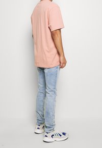 Camiseta de algodón rosa claro con un corte relajado, combinada con jeans desgastados azul claro y zapatillas blancas con acentos en azul y verde.