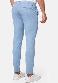 Pantaloni blu chiaro con una vestibilità slim, realizzati in un tessuto morbido. Presentano tasche posteriori con bottoni e tasche laterali. Abbinati a sneakers bianche.