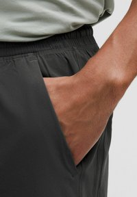 Grå atletiske shorts med elastisk talje og sidelomme, fremhæver et glat, let materiale og subtile syninger.