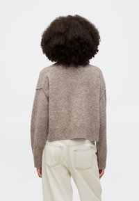 Supjaustytas megztinis šviesiai rudos spalvos, su raukšlėtu apvadu ir nuleistais pečiais. Su derančiomis aukštu liemeniu šviesiai geltonomis kelnėmis.