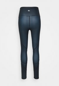 Leggings a vita alta di colore blu scuro con una texture liscia, forma aderente e dettagli di cuciture a pannello diagonali. Logo semplice in vita.