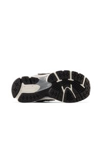 Semelle de chaussure de sport noire et grise présentant des rainures profondes pour une meilleure adhérence et une surface texturée. Comprend un logo et des éléments de design distincts.