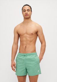 Pantaloni scurți de înot verzi, cu talie elastică și șnur în față; designul cu fața plată prezintă un logo alb pe piciorul stâng.