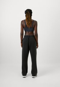 Juodas tamprus audinys sportinis liemenukas su reguliuojamomis petnešėlėmis, derinamas su laisvai krentančiomis juodomis sportinėmis kelnėmis, turinčiomis elastinį juosmenį ir raukiniais ant rankovių.