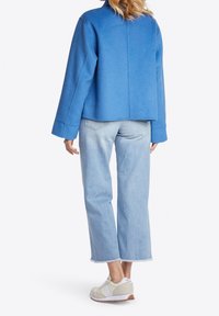 Blå kort jakke med brede ærmer, kombineret med lyseblå jeans med frynset kant. Hvide og lysegrå sneakers fuldender outfittet.