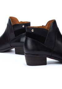 Bottes noires en cuir jusqu'à la cheville avec un petit talon empilé, silhouette épurée, agrémentées de panneaux lisses et texturés, présentant des clous en métal.