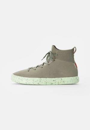 Basket montante tricotée en vert olive clair avec des lacets assortis et une semelle vert clair mouchetée sur fond blanc.