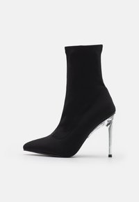 Sort ankelstøvle med en sok-lignende design, spids tå og gennemsigtig stiletthæl. Lavet af glat, strækbart stof med sømdetaljer.